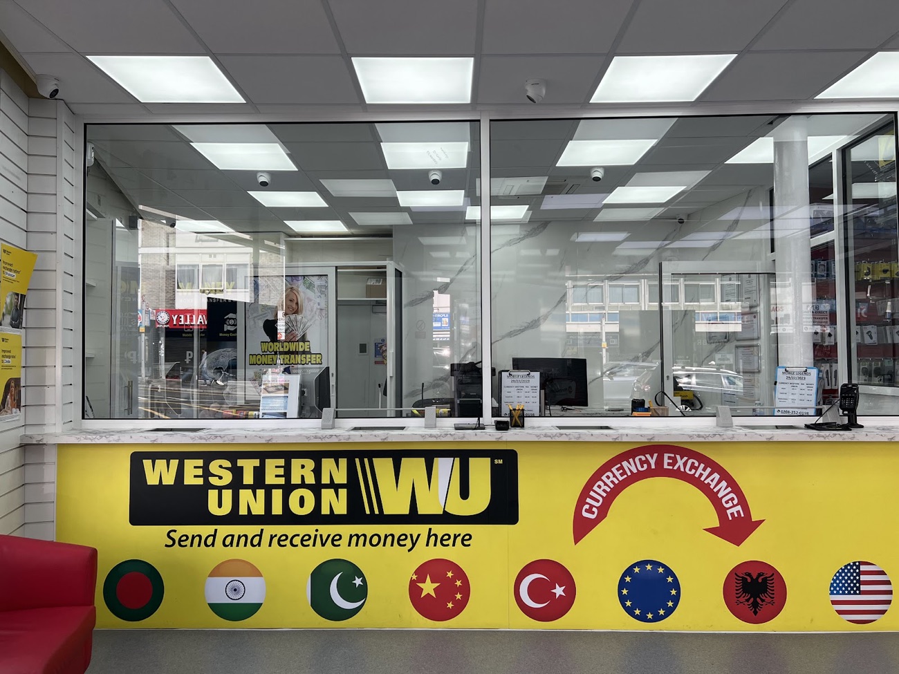 The Western Union and currency exchange counter inside Mobile Legends, Ilford, with a bright yellow 'Send and receive money here' facia.